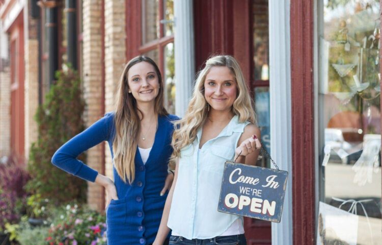 Young female business partners holding an open sign outside