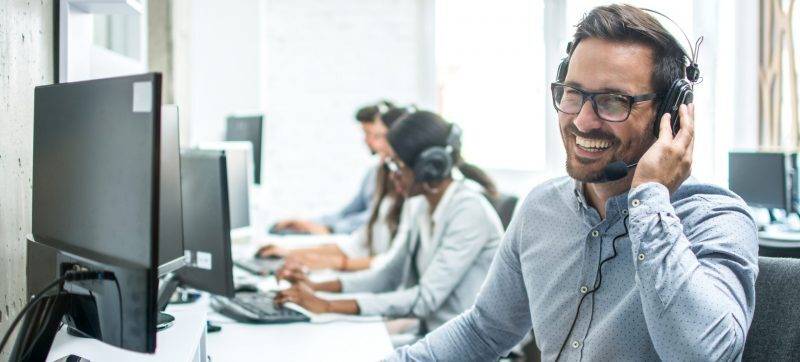 Smiling handsome customer support operator with headset working in call center.