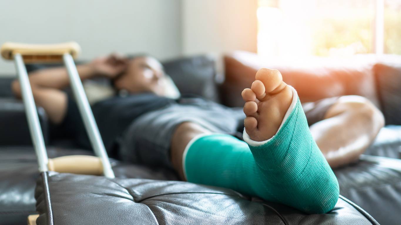 Bone fracture foot and leg on male patient with splint cast and crutches during surgery rehabilitation and orthopaedic recovery staying at home