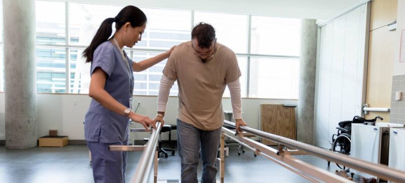 Male patient takes first steps using orthopedic parallel bars