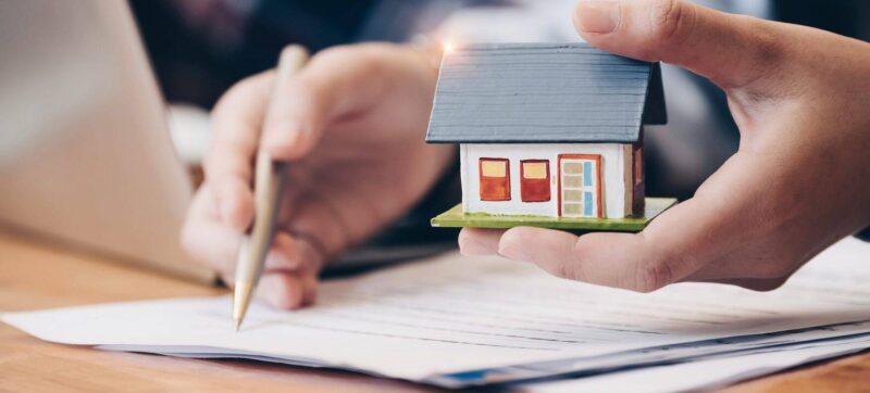 Close up real estate agent with house model hand putting signing contract,have a contract in place to protect it,signing of modest agreements form in office.Concept real estate,moving home or renting property