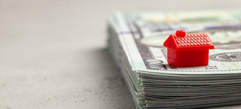 Red house on a stack of money. The concept of insurance or the purchase of real estate.